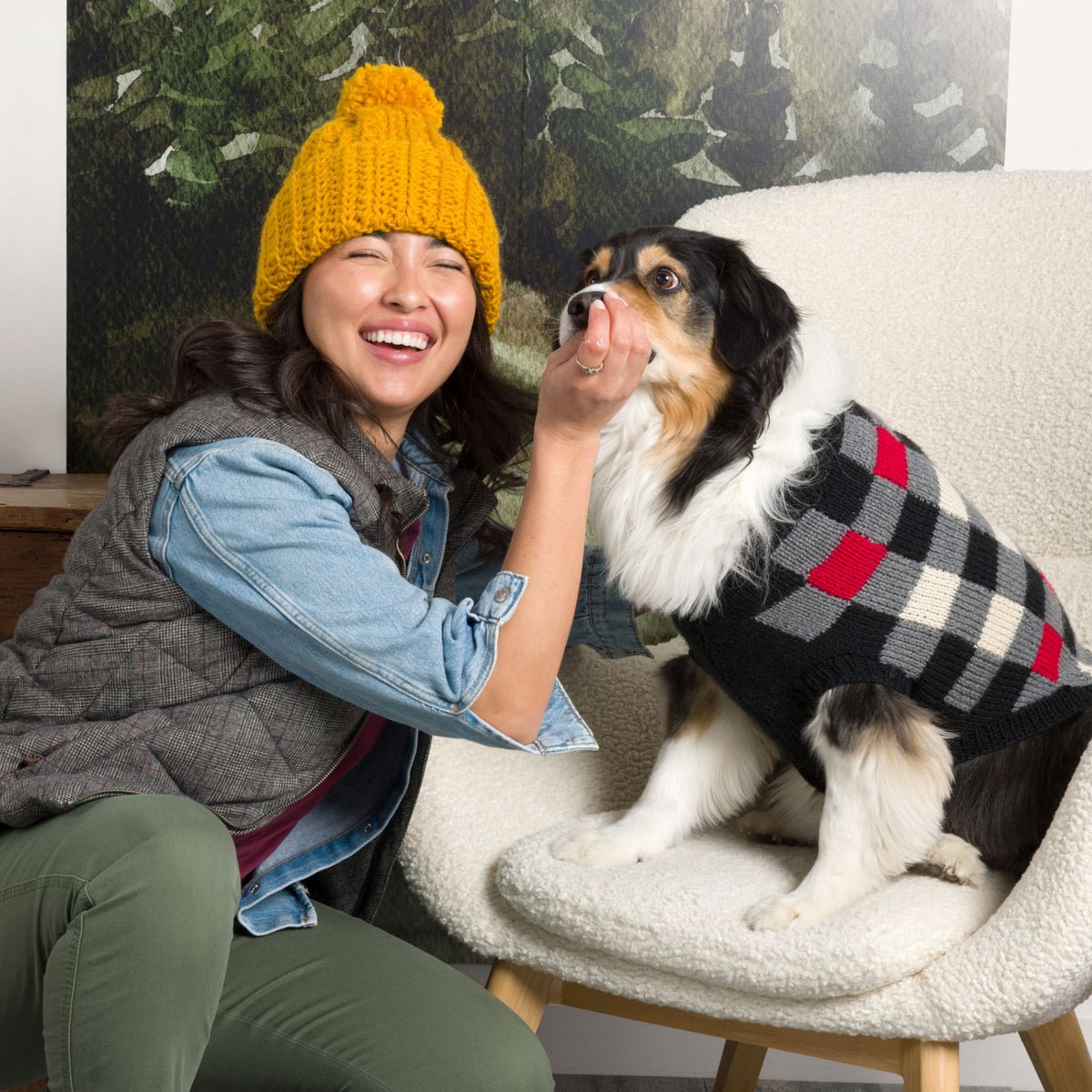 Woman in yellow knit hat with dog in checkered sweater, showcasing Patons' Great Outdoors collection.