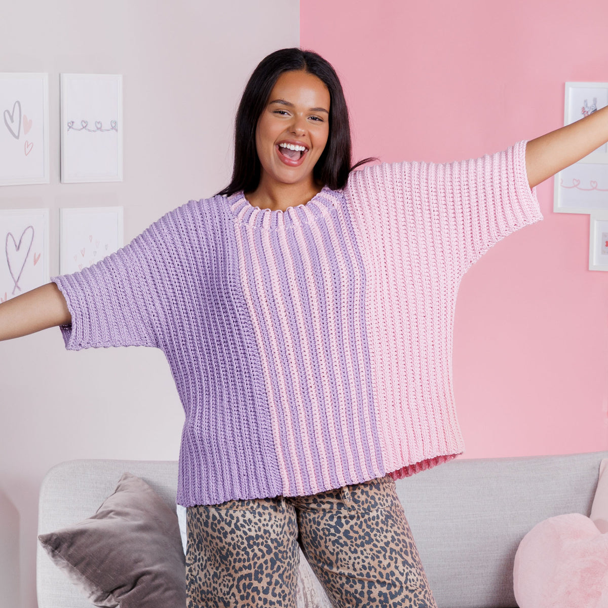 Woman wearing a purple and pink striped crochet sweater in a room with a pink and white wall.
